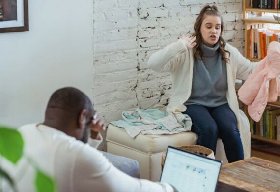 A woman gesturing to a man who is looking at his laptop