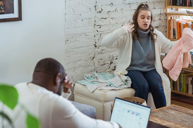 A woman gesturing to a man who is looking at his laptop 